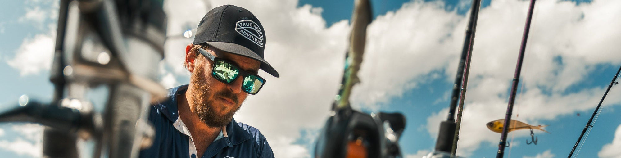 Store locator banner: A man wearing a black cap with a white logo and a navy blue polo shirt, standing outdoors on a boat with fishing rods.